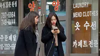 Dua wanita berbincang sambil berjalan di sepanjang jalan di Seoul, Korea Selatan (19/2). (AFP Photo/David Gannon)