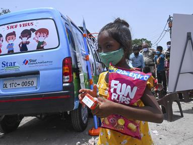 Seorang gadis pergi dengan makanan ringan setelah memberikan sampel swab untuk menguji virus corona Covid-19 di dalam sebuah van di New Delhi, India (1/7/2021).  Kegiatan ini diselenggarakan oleh Polisi Delhi bekerja sama dengan lab Star Imaging and Path. (AFP/Prakash Singh)