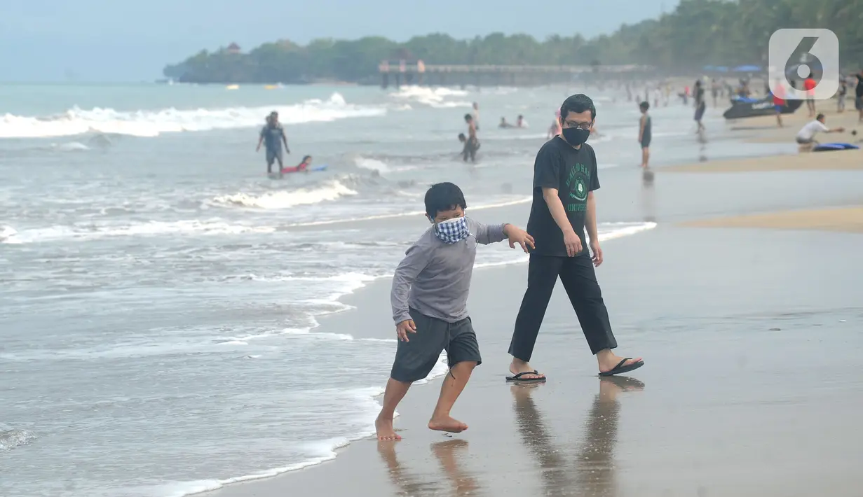 Wisatawan yang mengenakan masker bermain air saat mengunjungi Pantai Anyer di Cilegon, Banten, Minggu (25/10/2020). Akhir pekan dimanfaatkan warga Jakarta dan sekitarnya untuk berwisata dengan tetap menerapkan protokol kesehatan Covid-19. (merdeka.com/Arie Basuki)