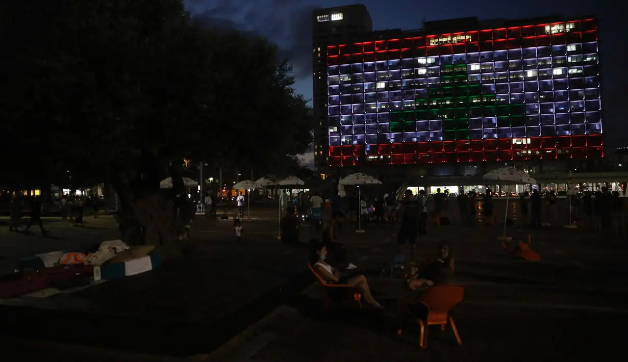 Warga Israel duduk ketika gedung Balai Kota diterangi dengan bendera Lebanon di Tel Aviv, Rabu (5/8/2020). Cahaya bendera Lebanon diproyeksikan sebagai bentuk solidaritas atas ledakan dahsyat di Beirut yang menghebohkan dunia. (AP Photo/Sebastian Scheiner)