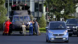 Petugas servis bersiap memindahkan helikopter Black Hawk militer AS yang mendarat darurat di boulevard yang sibuk, di Bucharest, Kamis (15/7/2201). Helikopter yang ambil bagian dalam persiapan hari Penerbangan Rumania itu mendarat darurat karena masalah teknis. (AP Photo/Andreea Alexandru)