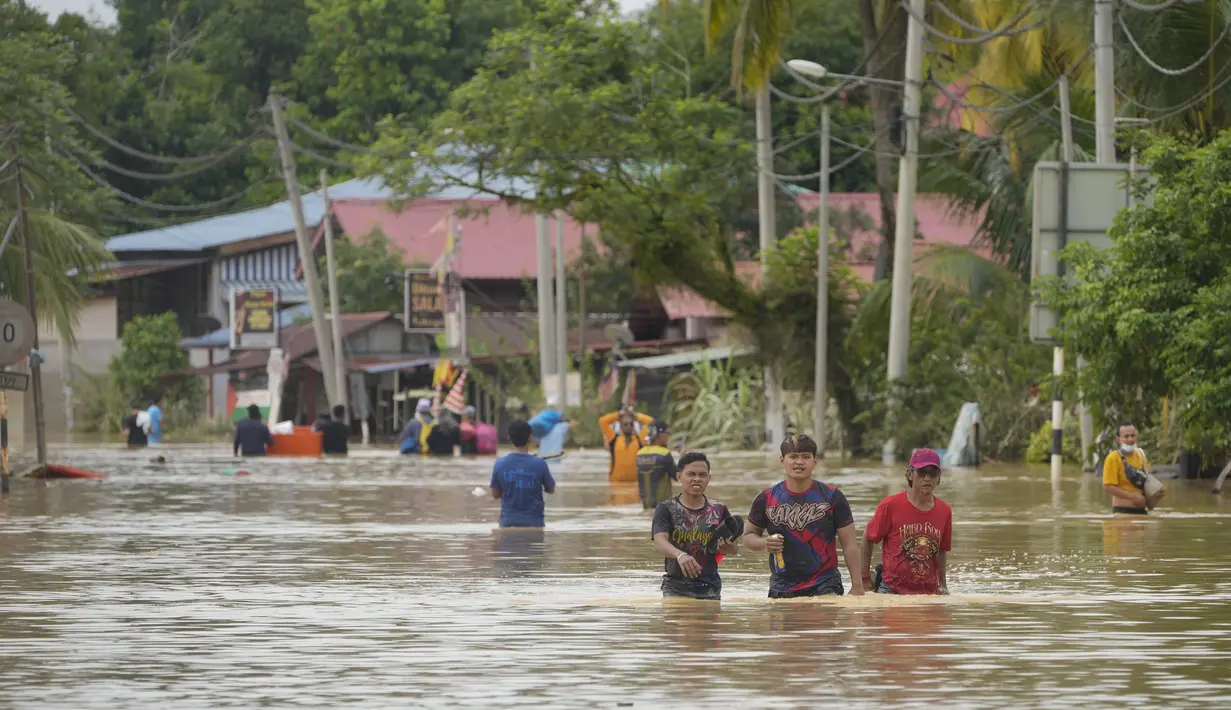 Warga mengarungi jalan yang dilanda banjir di Hulu Langat, luar Kuala Lumpur, Malaysia, Minggu  (19/12/2021). Kuala Lumpur dan perkampungan sekitarnya dilanda banjir akibat hujan deras selama dua hari, menyebabkan ribuan warga mengungsi dan banyak jalan yang memutus akses. (Foto AP/Vincent Thian)