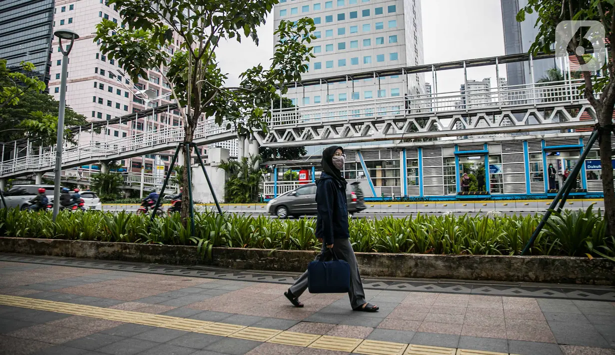 Seorang perempuan melintasi trotoar di Jalan Sudirman, Jakarta Pusat, Rabu (6/1/2021). Selama pembatasan sosial berskala besar (PSBB) di wilayah Jawa dan Bali pada 11-25 Januari 2021, aktivitas bekerja di kantor diperketat dengan sistem work from home (WFH) 75 persen. (Liputan6.com/Faizal Fanani)