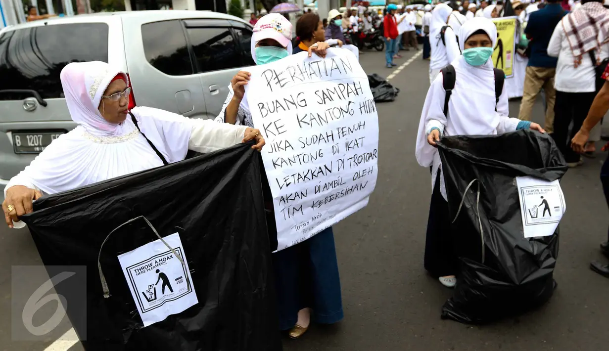 Sejumlah relawan membawa kantong plastik besar dan spanduk bertuliskan "Throw A HOAX, Here Please" di tengah aksi damai 4 November di Jakarta, Jumat (4/11). Mereka mengumpulkan sampah yang dibuang anggota ormas. (Liputan6.com/Faizal Fanani)