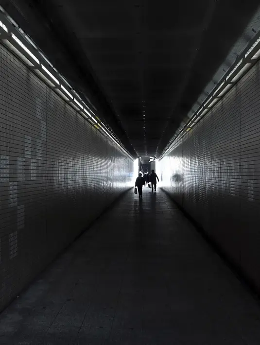 Orang-orang yang mengenakan masker pelindung untuk membantu mengekang penyebaran virus corona berjalan melalui underpass di Tokyo, Selasa (26/1/2021). Jepang mengonfirmasi lebih dari 1.000 kasus Virus Corona baru pada 26 Januari 2021. (AP Photo/Eugene Hoshiko)