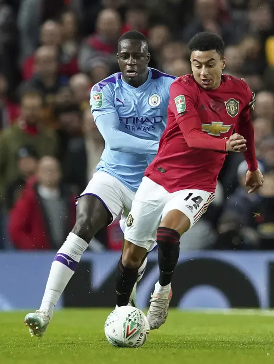 Penyerang Manchester United, Jesse Lingard membawa bola dari kejaran Bek Manchester City, Benjamin Mendy pada pertandingan leg pertama semifinal Piala Liga Inggris di Old Trafford (7/1/2020). City menang 3-1 atas MU. (AP Photo / Jon Super)
