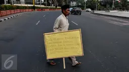 Syaripudin Dodo (59) melakukan aksi dengan membawa poster di Bundaran HI, Jakarta, Kamis (30/7/2015). Kakek ini meminta pertolongan pengguna jalan untuk membiayai sekolah cucunya di Perguruan Islam Al Masthuriyah Sukabumi. (Liputan6.com/Johan Tallo)