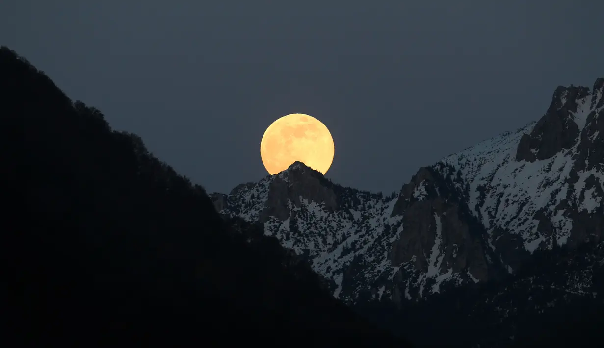 Bulan purnama tampak di belakang pegunungan Alpen yang tertutup salju di Buching, Jerman selatan, (10/5). (Karl-Josef Hildenbrand/dpa/AFP)