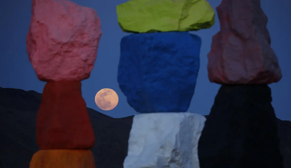 Supermoon terlihat dari celah instalasi seni Seven Magic Mountains karya seniman Ugo Rondinone di Las Vegas, Amerika Serikat, Selasa (7/4/2020). Seven Magic Mountains terdiri dari tujuh buah bangunan yang disusun dari batuan besar warna-warni. (AP Photo/John Locher)
