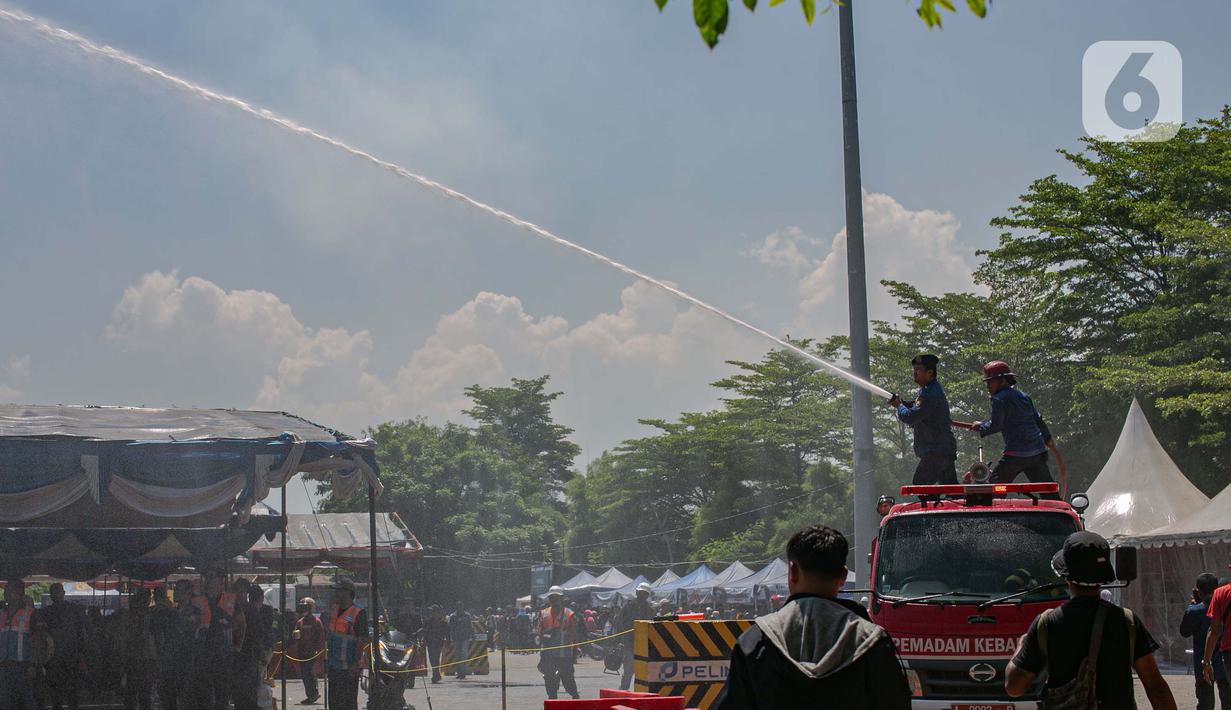 Petugas pemadam kebakaran melakukan penyiraman air ke tenda para pemudik motor di Pelabuhan Ciwandan, Banten, Minggu (7/4/2024). (Liputan6.com/Angga Yuniar)