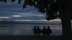 Orang-orang menikmati matahari terbenam di danau Chiemsee di Chieming, Jerman, Selasa, (25/8/2020). Chiemsee terbagi menjadi dua bagian, yaitu bagian timur laut yang lebih besar yang disebut Weitsee serta bagian Inselsee yang terletak di barat daya. (AP Photo / Matthias Schrader)