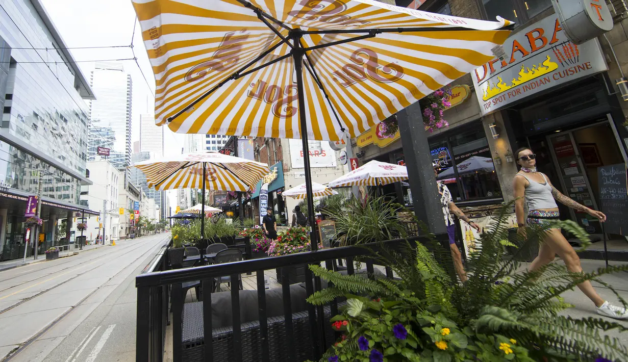 Sejumah orang melewati area makan terbuka sebuah restoran di Toronto, Kanada, 18 Juli 2020. Kota Toronto meluncurkan program CafeTO yang memungkinkan restoran dan bar memperluas area makan terbuka mereka guna melayani lebih banyak pelanggan dengan aman selama pandemi COVID-19. (Xinhua/Zou Zheng)