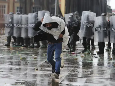 Seorang pria melarikan diri dari polisi setelah melemparkan batu ke arah mereka selama pemogokan nasional untuk memprotes reformasi pajak yang diusulkan pemerintah, di Bogota, Kolombia, Rabu (28/4/2021). (AP Photo/Fernando Vergara)