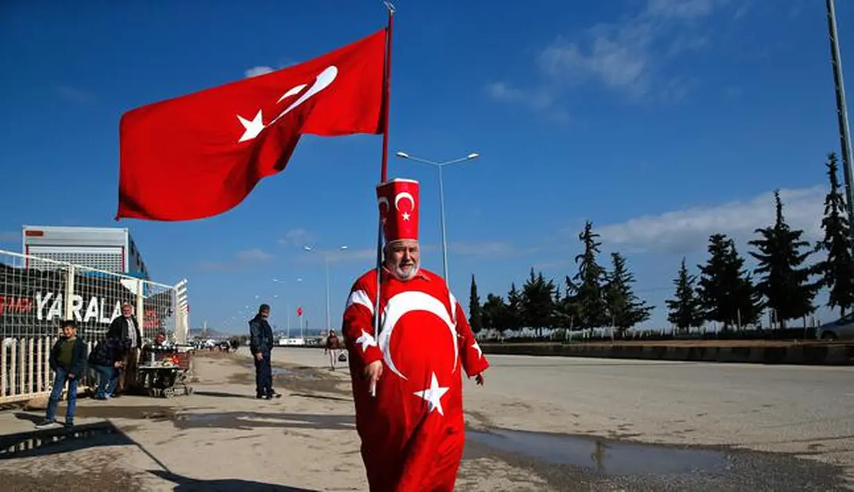 Isikli Tosun Baba (60) memegang dan mengenakan bendera Turki di Oncupinar, Kilis, Turki, Minggu (28/1). (AP Photo/Lefteris Pitarakis)