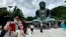 Sepasang pengunjung berswafoto dengan latar belakang The Great Buddha atau yang biasa disebut Kamakura Daibutsu di kuil Kotoku-in di Kamakura, Prefektur Kanagawa, Jepang, Sabtu (20/6/2020). Patung Buddha yang menjulang dengan tinggi 13,35 meter ini didirikan tahun 1252. (Behrouz MEHRI/AFP)