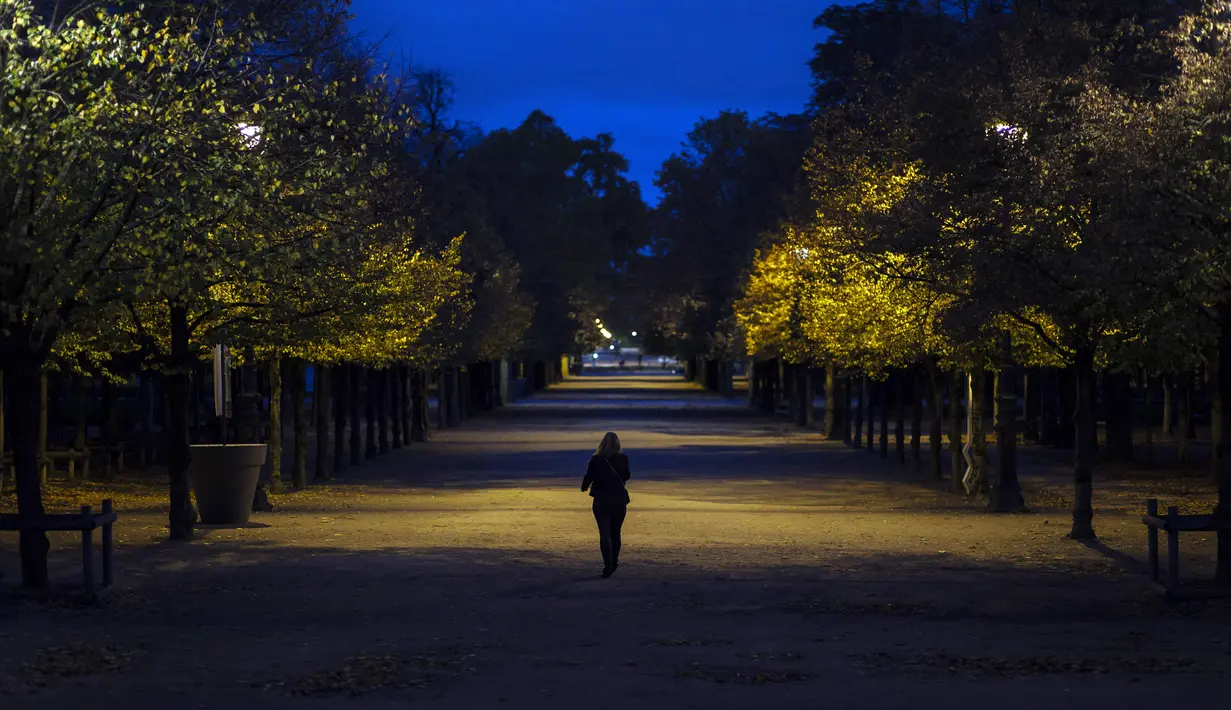 Seorang wanita berjalan di taman Tuileries yang kosong di pusat kota Paris (30/1/2020). Prancis memberlakukan kembali penguncian nasional selama sebulan yang bertujuan untuk memperlambat penyebaran virus, menutup semua bisnis yang tidak penting dan melarang orang masuk. (AP Photo/Lewis Joly)