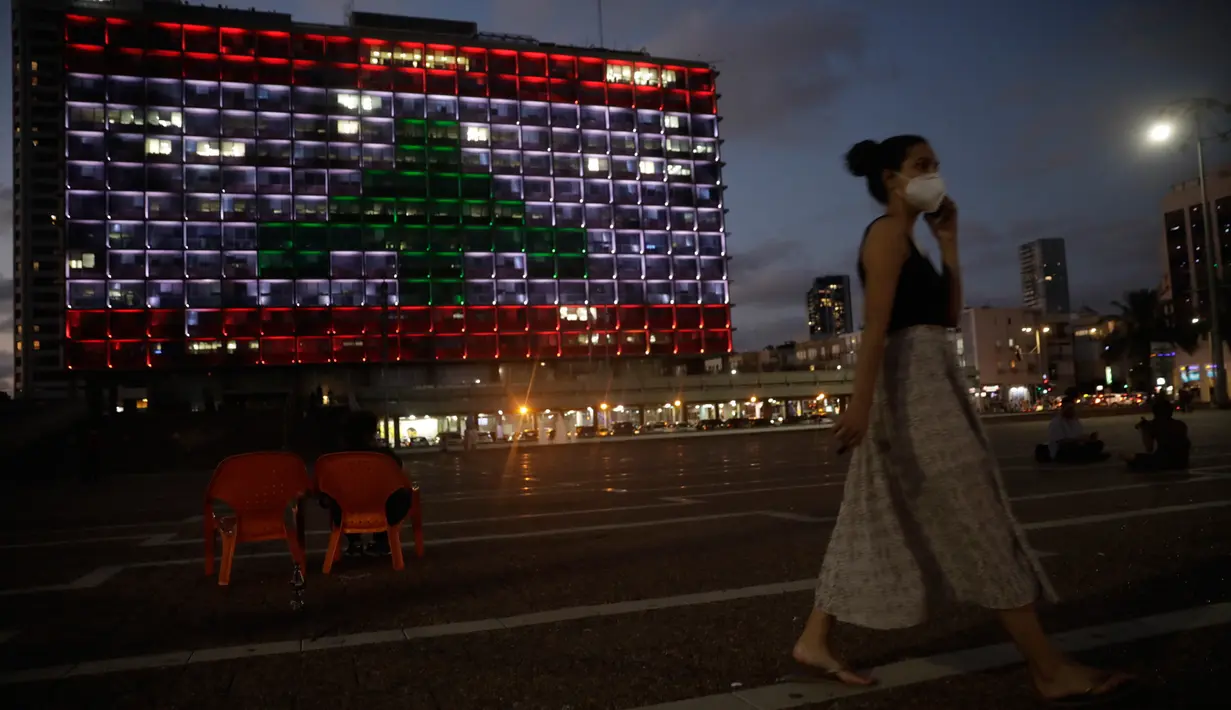 Seorang perempuan Israel berjalan saat Gedung Balai diterangi dengan bendera Lebanon di Tel Aviv, Rabu (5/8/2020). Cahaya bendera Lebanon diproyeksikan sebagai bentuk solidaritas atas ledakan dahsyat di Beirut yang menghebohkan dunia. (AP Photo/Sebastian Scheiner)