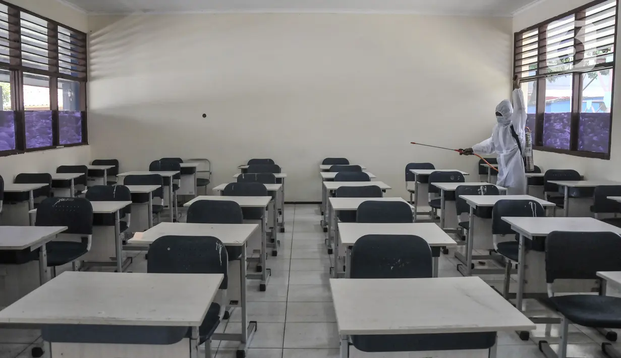 Petugas sekolah menyemprotkan disinfektan di ruang kelas usai Pembelajaran Tatap Muka (PTM) 100 persen di SMP Negeri 9 Depok, Senin (24/1/2022). Pihak sekolah melakukan penyemprotan disinfektan secara rutin seiring dimulainya pelaksanaan PTM 100 persen di Depok. (merdeka.com/Iqbal S Nugroho)