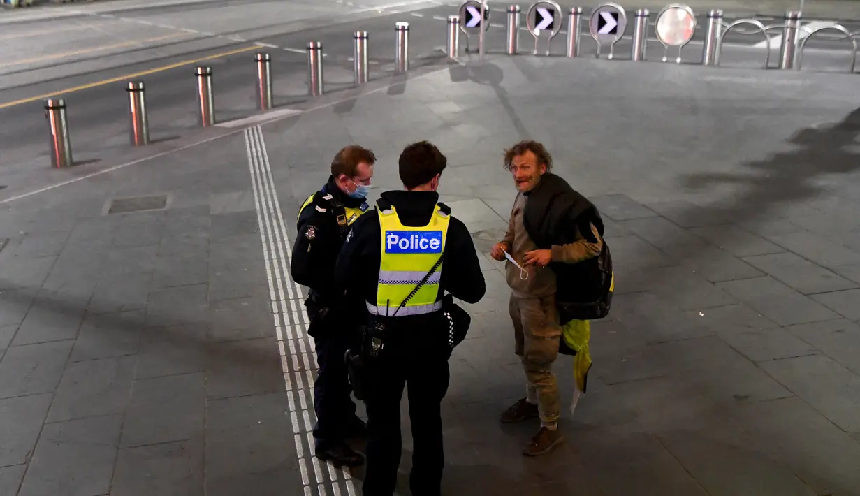 Polisi berbicara dengan seorang pejalan kaki selama aturan jam malam di Melbourne, pada Selasa (17/8/2021). Kota terbesar kedua di Australia itu memberlakukan pembatasan tinggal di rumah pada pukul 9 malam hingga 5 pagi untuK meredam lonjakan Covid-19 varian Delta. (William WEST/AFP)