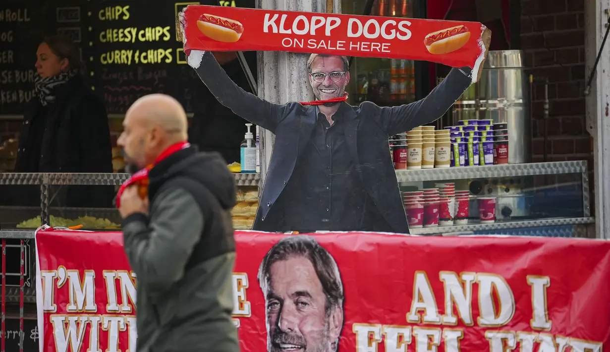 <p>Seorang pedagang Hot Dogs memakai topeng pelatih Liverpool, Jurgen Klopp sambil membentangkan syal saat laga putaran keempat Piala FA antara Liverpool melawan Norwich City di Anfield, Liverpool, Inggris, Minggu (28/01/2024). (AP Photo/Jon Super)</p>
