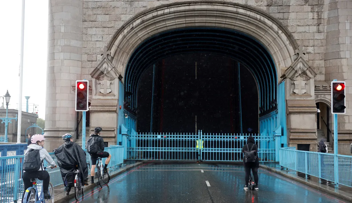 Pesepeda menunggu untuk menyeberangi Tower Bridge yang terjebak dalam posisi terbuka di pusat kota London Senin (9/8/2021). Tower Bridge London macet terbuka mengakibatkan gangguan lalu lintas di kedua sisi Sungai Thames karena mobil dan pejalan kaki tidak dapat menyeberang. (Tolga Akmen/AFP)