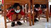 Anak-anak sekolah berlindung di bawah meja untuk melindungi diri mereka sat latihan gempa dan tsunami di Tanjung Benoa, Kabupaten Badung, Bali, 24 Mei 2022. (SONY TUMBELAKA/AFP)