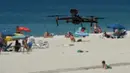 Sebuah drone atau pesawat tak berawak yang diterbangkan oleh polisi setempat memperingatkan orang-orang untuk menjaga jarak di pantai Areas di Sanxenxo, Spanyol, Selasa (14/7/2020). Drone tersebut untuk memantau jaga jarak antarwisatawan saat berlibur di masa pandemi Corona. (MIGUEL RIOPA / AFP)