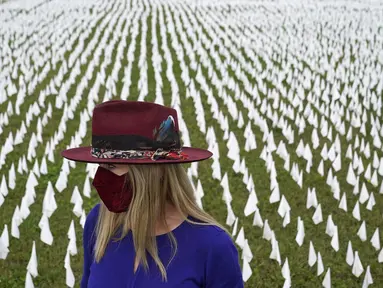 Seniman Suzanne Brennan Firstenberg berdiri di antara ribuan bendera putih yang ditanam untuk mengenang warga Amerika yang meninggal karena COVID-19 di dekat Stadion RFK di Washington, Selasa (27/10/2020). Instalasi seni publik ini disebut "In America, How Could This Happen.” (AP/Patrick Semansky)