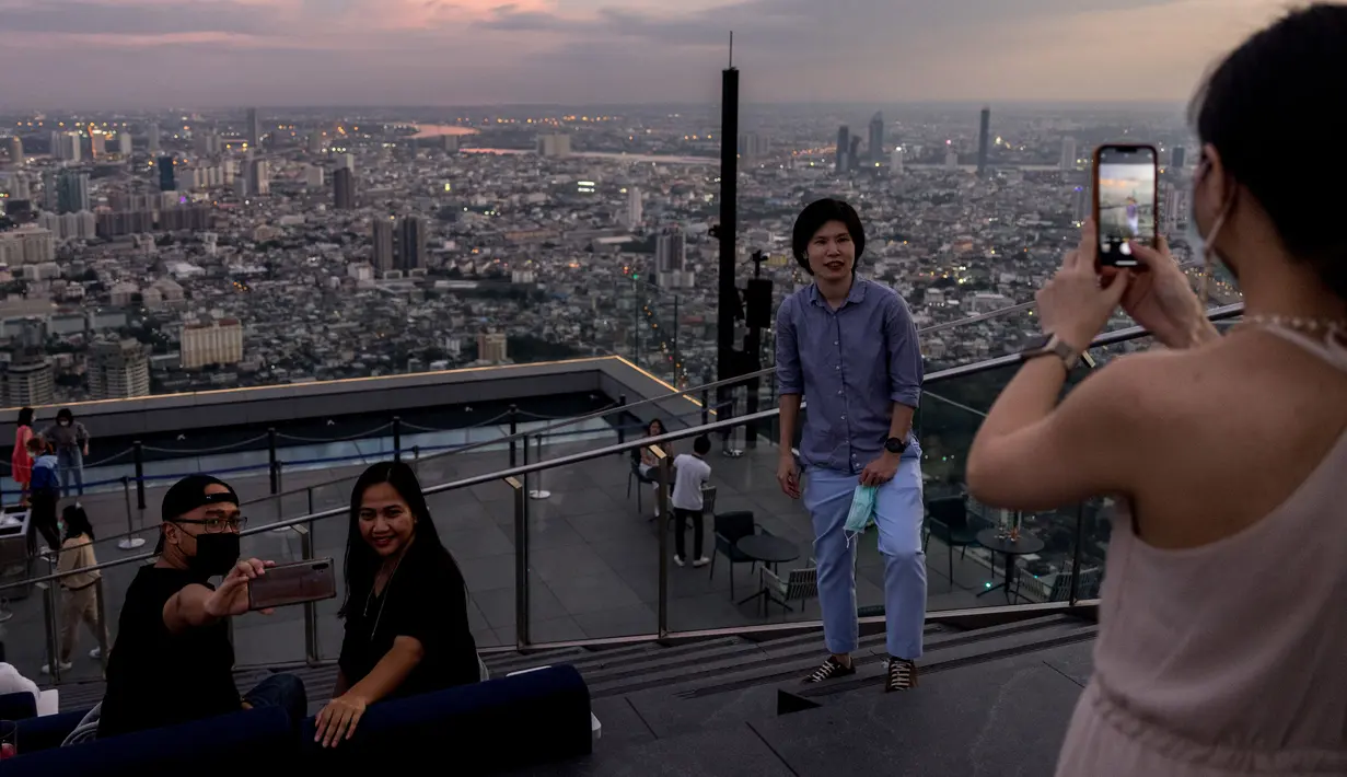 Orang-orang berfoto dari dek observasi di gedung pencakar langit King Power Mahanakhon saat matahari terbenam di Bangkok, Thailand pada 25 Oktober 2021. Gedung yang dibuka pada tahun 2017 lalu ini memiliki 77 lantai dengan tinggi 324 meter. (Jack TAYLOR / AFP)