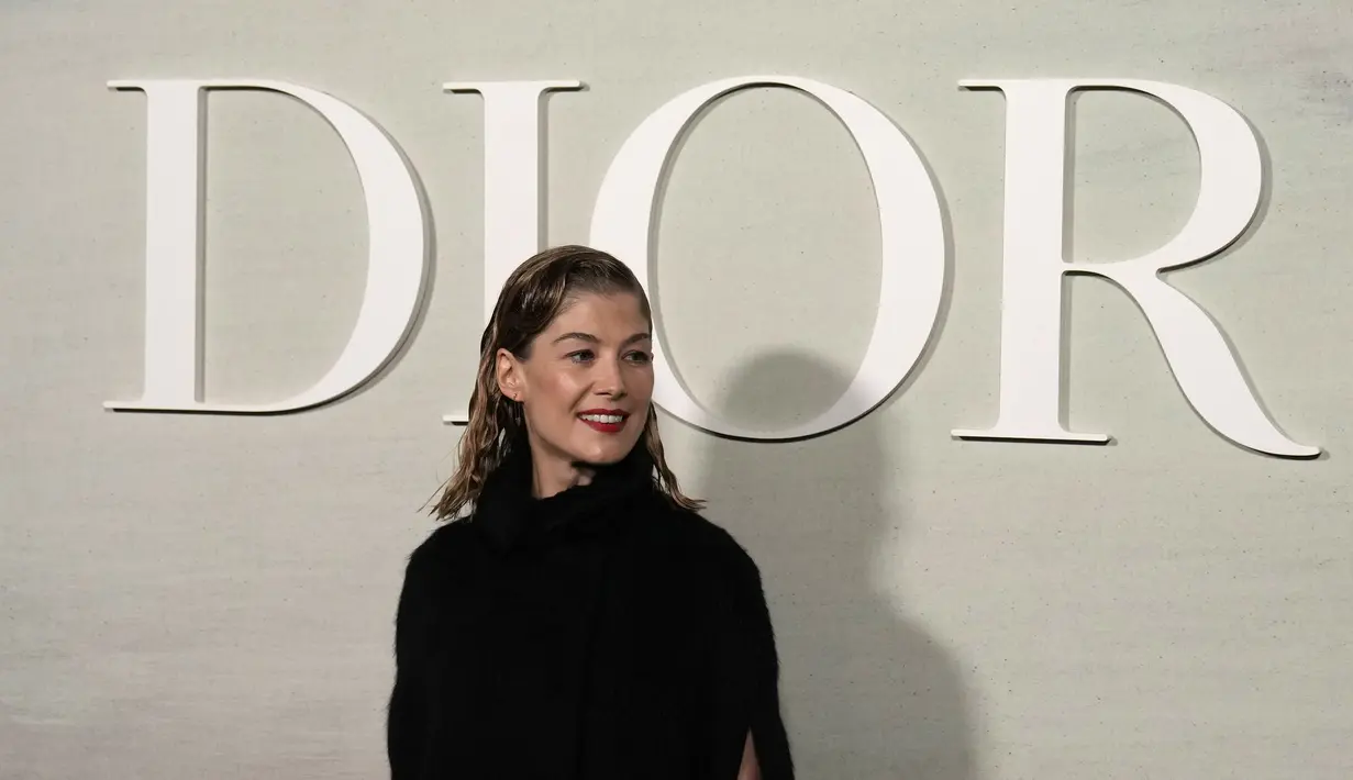 Rosamund Pike berpose di depan koleksi busana siap pakai Musim Semi/Musim Panas 2023 Dior yang disajikan di Paris, Selasa, 27 September 2022. Rosamund Pike menarik perhatian dalam gaun renda hitam yang ia kenakan di bawah jaket bulu palsu tanpa lengan. (AP Photo/Francois Mori)