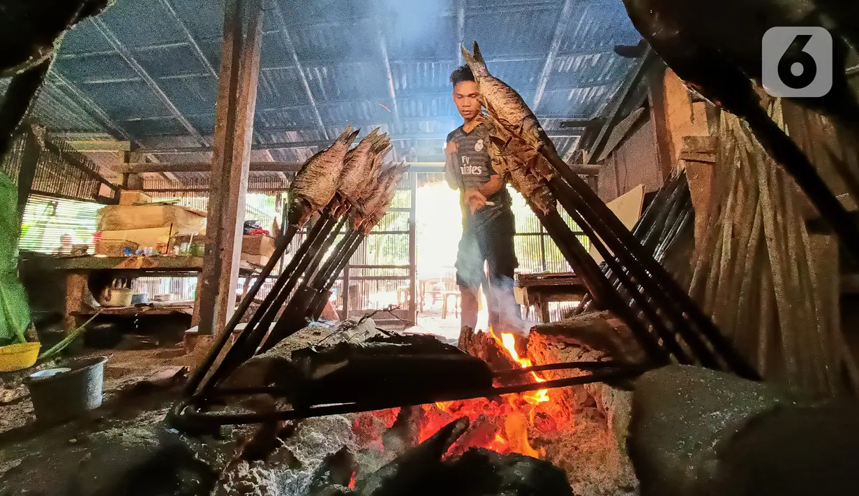 Karyawan mengasap ikan mas menggunakan kayu bakar di Setu Tujuh Muara Sawangan, Depok, Minggu (19/06/2022). Proses pengasapan ikan yang memakan waktu sekitar 7 jam ini harus dipesan 1-2 hari sebelum disantap dan dijual dengan harga Rp85.000 per kilogram. (Liputan6.com/Fery Pradolo)