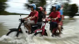 Pengendara motor melintasi jalan yang terkena banjir di kawasan Jal Besar, Malaysia, Kamis (5/1). Sekitar 23 ribu orang terpaksa mengungsi karena banjir yang disebabkan hujan muson ini. (AFP PHOTO / MOHD RASFAN)