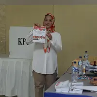 Saat mendatangi TPS, Rachel tampil dengan baju lengan panjang warna putih dengan penutup kepala. Ibu dari Muhammad Kale Mata Angin menunjukkan surat suara sebelum melakukan pencoblosan. (Nurwahyunan/Bintang.com)
