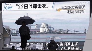 Orang-orang berjalan di depan monitor besar program berita yang menyerukan penghematan listrik di Tokyo, Selasa (22/3/2022). Pemerintah Jepang memperingatkan potensi pemadaman karena kekurangan pasokan listrik akibat tutupnya beberapa pembangkit setelah gempa bumi pekan lalu. (Kyodo News via AP)