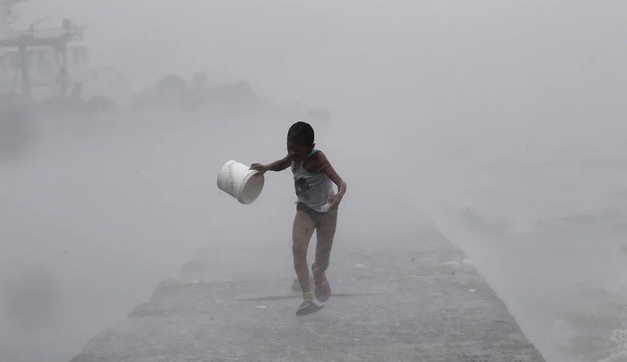 Seorang anak laki-laki berlari di tengah hujan lebat saat badai topan Linfa disertai gelombang laut menghantam Teluk Manila, Filipina, Senin (6/7/2015). Akibat badai aktivitas penerbangan, pelabuhan dan sekolah-sekolah ditutup. (REUTERS/Romeo Ranoco)
