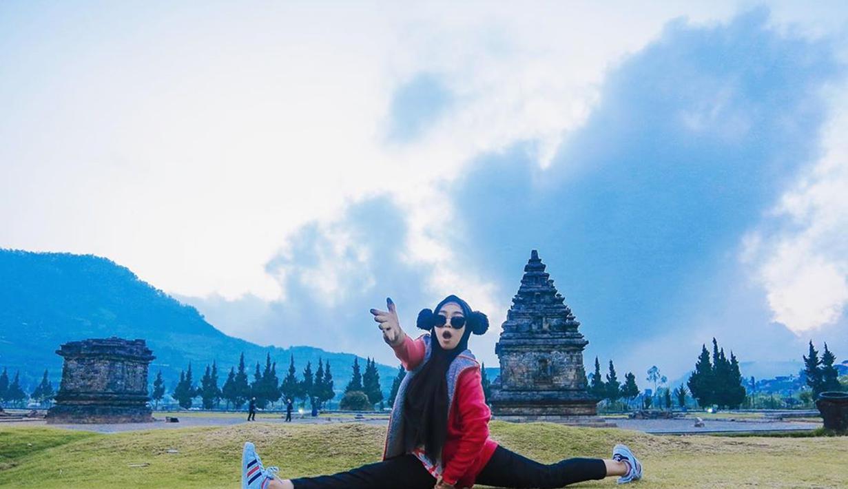 Gadis kelahiran Batam ini merentangkan kedua kakinya dan menunjukkan ekspresi yang lucu saat liburan di Dieng. Dengan pakaian serba hitam, ditambah dengan jaket merah dan sepatu putih, ia berpose di depan sebuah bangunan candi. (Liputan6.com/IG/@riaricis1795)