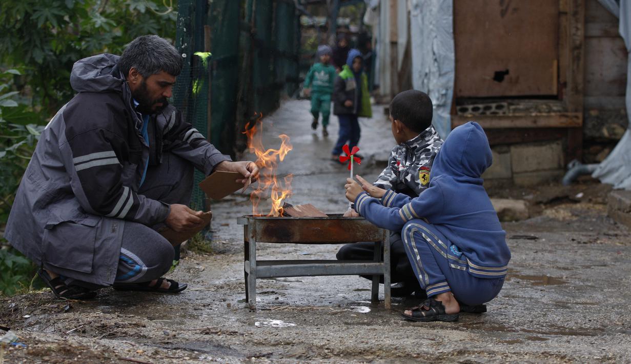 Sebuah keluarga pengungsi Suriah menghangatkan diri di sekitar api di sebuah kamp pengungsi di kota pelabuhan selatan Sidon, Lebanon pada 19 Januari 2022. Badai salju di Timur Tengah telah membuat banyak warga Lebanon dan Suriah berebut mencari cara untuk bertahan hidup. (AP Photo/Mohammed Zaatari)