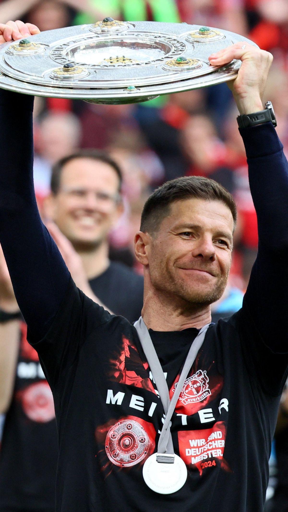 Senyum Xabi Alonso mengangkat trofi juara Bundesliga 2023/2024 yang diraih Bayer Leverkusen. Foto:&nbsp;REUTERS/Wolfgang Rattay