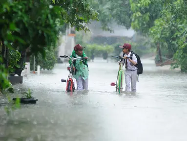 Dua anak sekolah membawa sepedanya melitasi banjir di perumahan Pondok Hijau Permai, Bekasi, Senin (20/2). Hujan berkepanjangan menyebabkan kali yang melintasi perumahan tersebut meluap. (Liputan6.com/Gempur M. Surya)