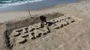 Seorang seniman Palestina mengukir kata "TETAP DI RUMAH TETAP AMAN" dengan pasir di sebuah pantai di Gaza City pada 12 April 2020. Palestina pada Minggu (12/4) melaporkan jumlah total kasus COVID-19 di negara tersebut telah mencapai 290. (Xinhua/Rizek Abdeljawad)