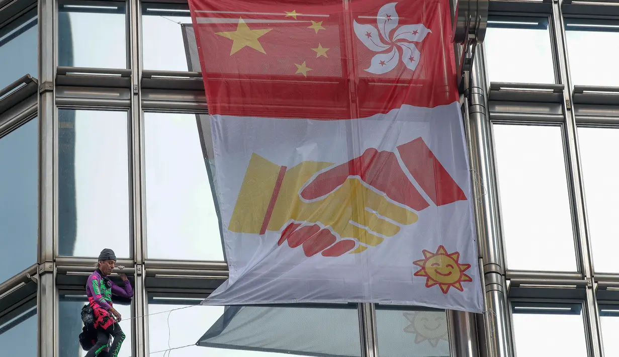 Alain Robert yang dijuluki 'French Spiderman' mengibarkan bendera China dan Hong Kong di gedung pencakar langit Cheung Kong Center, Hong Kong, Jumat (16/8/2019). Selama pendakian, Alain Robert memasang spanduk yang menampilkan bendera Hong Kong dan China. (AP Photo/Vincent Thian)