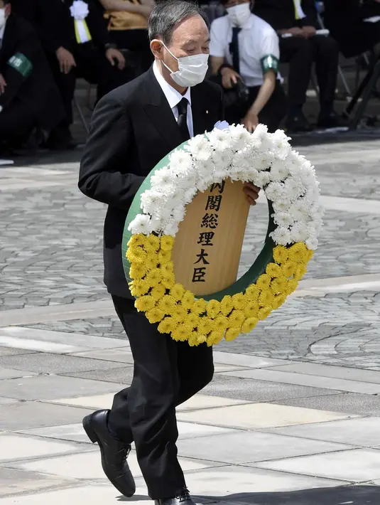 Perdana Menteri Jepang Yoshihide Suga membawa karangan bunga selama upacara di Nagasaki Peace Park di Nagasaki, Jepang selatan, Senin (9/8/2021). Kota Nagasaki di Jepang pada hari Senin menandai peringatan ke-76 bom atom AS. (Kyodo News via AP)