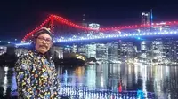 Yogi menggunakan baju khas Jawa pada Senin malam sambil mengabadikan momen bersejarah dengan jembatan Brisbane yang berwarna merah putih. (Facebook. Agustinus Jogiono)