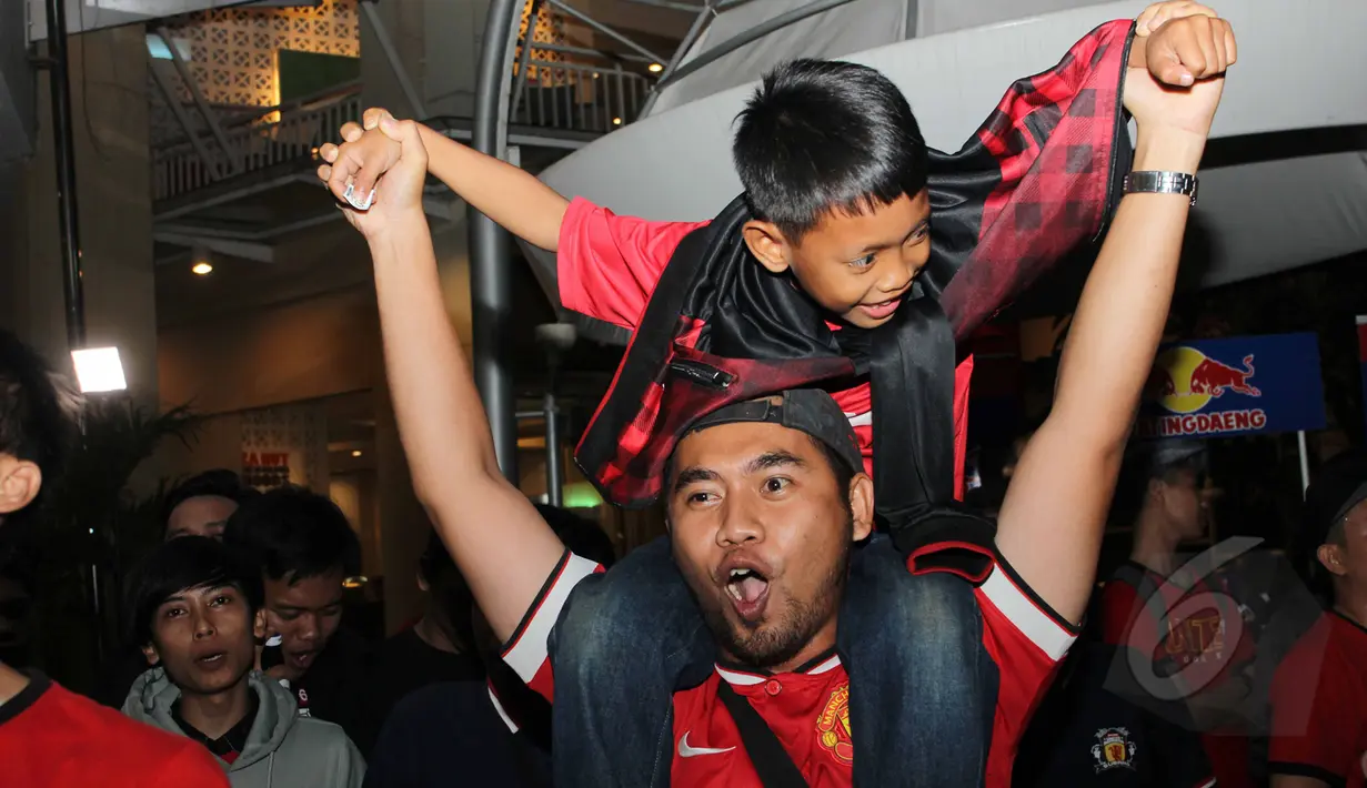 Seorang pendukung Manchester United mengendong seorang anak saat nonton bola seru Manchester United vs Arsenal di Karawang Central Plaza, Minggu (17/5/2015). Laga antara Manchester United dan Arsenal berakhir imbang. (Liputan6.com/Helmi Afandi)