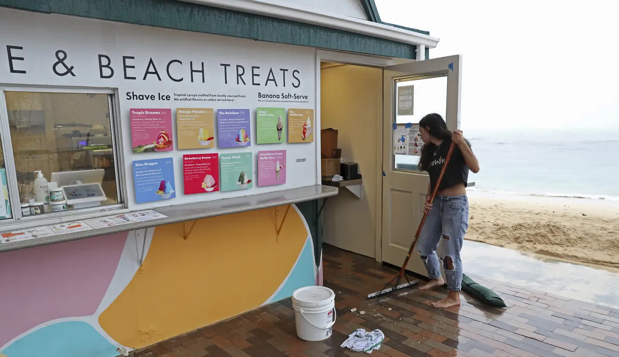 Calista Cafiero menyapu air hujan dari toko yang dikelolanya di Pantai Waikiki, Honolulu  (6/12/2021). Pihak berwenang mengatakan kondisi yang berpotensi lebih buruk ke depannya. (AP Photo/Marco Garcia)