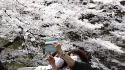 Orang-orang yang memakai masker berfoto selfie bersama, saat mereka melihat bunga sakura mekar penuh di Taman Chidorigafuchi di Tokyo, Jepang, Senin (28/3/2022). (AP Photo/Koji Sasahara)