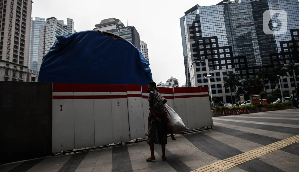 Warga melintas di dekat proyek Pembangunan tugu sepeda di Jalan Jenderal Sudirman, Jakarta, Rabu (30/3/2022). Tugu yang dulu sempat boming dan digembar-gemborkan kini terlihat terhenti pengerjaannya dan hanya ditutup terpal. (Liputa6.com/Johan Tallo)