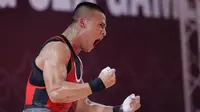 Selebrasi atlet Indonesia, Rizki Juniansyah, setelah berhasil memenangkan laga pada cabang angkat besi 73 Kg putra SEA Games 2023 di Phnom Penh, Kamboja, Minggu (14/5/2022). Hasil tersebut tidak hanya membawa Rizki menorehkan medali emas, tapi ia juga memecahkan tiga rekor SEA Games. (Bola.com/Abdul Aziz)