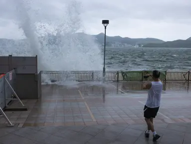 Seorang pria melihat ombak di kawasan pejalan kaki selama topan di Hong Kong, Senin (17/7/2023). Sekolah dan pasar saham ditutup di Hong Kong pada hari Senin karena Topan Talim menyapu selatan kota. (AP Photo/Louise Delmotte)