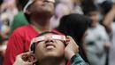 Pengunjung mengamati gerhana matahari cincin memakai kacamata khusus di Planetarium Taman Ismail Marzuki, Jakarta, Kamis (26/12/2019). Planetarium menyediakan sekitar 10 teleskop dan kacamata khusus agar pengunjung bisa menyaksikan gerhana matahari cincin dengan aman. (Liputan6.com/Faizal Fanani)
